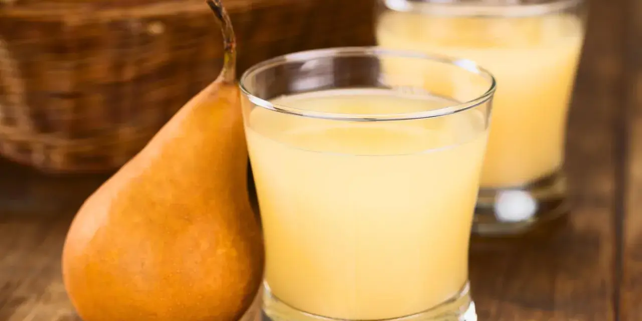 Frisch gepresster birnensaft selber machen ist einfach! Eine reife Birne neben einem Glas des köstlichen Saftes.