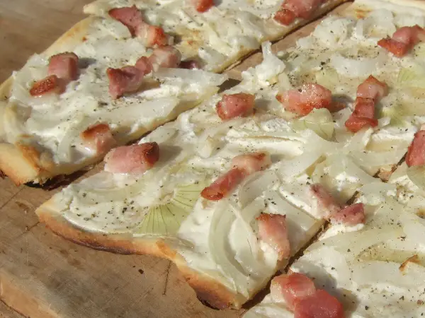 Flammkuchen mit dünnen Zwiebelringen und Speckwürfeln auf Crème fraîche. Ein köstlicher Belag für den knusprigen Teig.