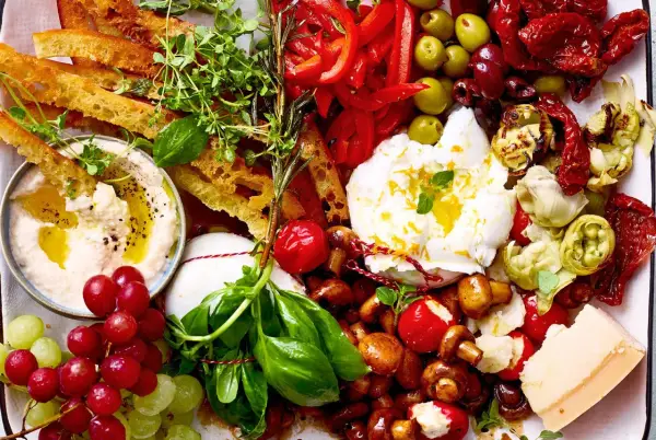 Eine Platte mit geilen Snacks: Hummus, Burrata, Trauben, Brot, Oliven, Pilze, Tomaten und Käse.