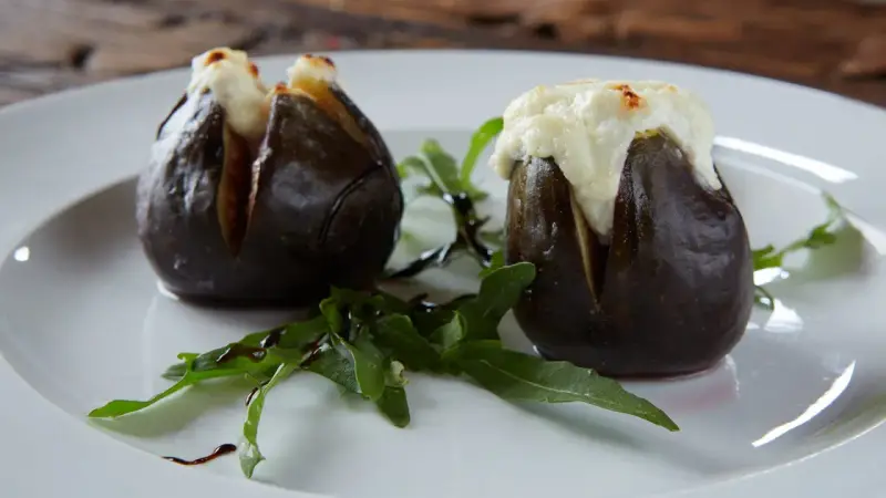 Zwei gefüllte Feigen, die auf einem Teller mit Rucola und Balsamico-Glasur liegen. Ein köstliches Gericht, das zeigt, wie man Feigen grillen kann.