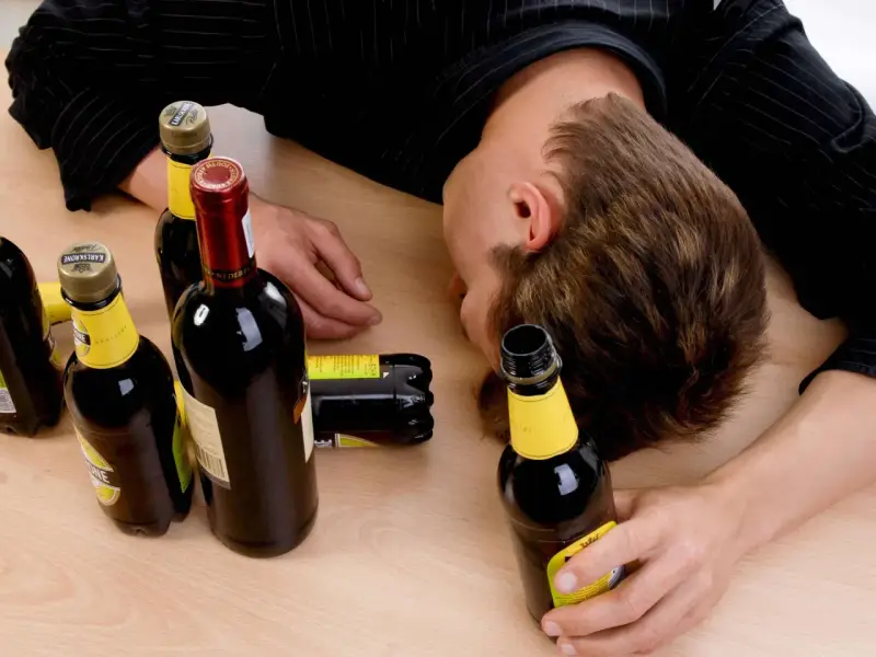Ein Mann liegt bewusstlos auf einem Tisch, umgeben von leeren Flaschen. Der Gedanke, dass **Whisky gesund** sein könnte, ist hier wohl fehl am Platz.