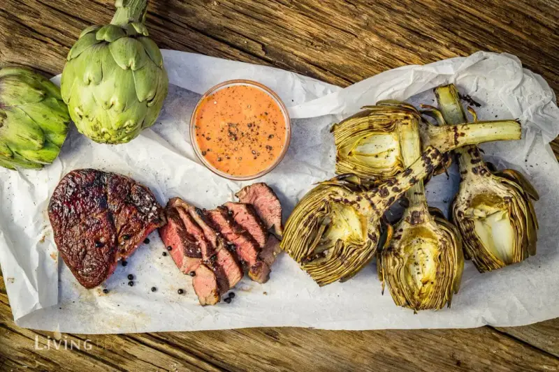 Saftiges Steak und gegrillte Artischocken mit Dip auf Holzuntergrund.