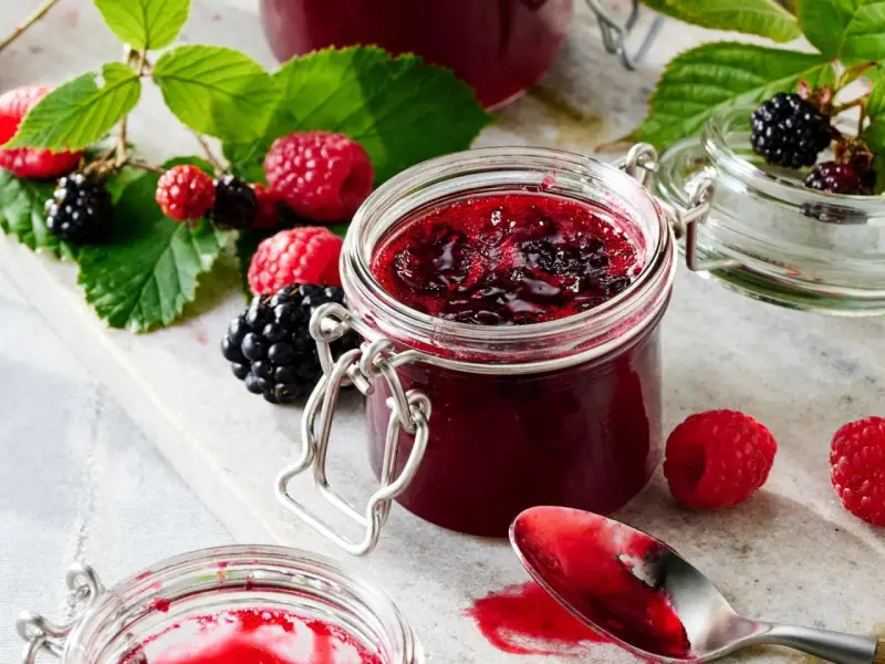 Frische Brombeeren und Himbeeren neben einem Glas selbstgemachter Marmelade. Perfekt für brombeeren rezepte schnell und einfach.