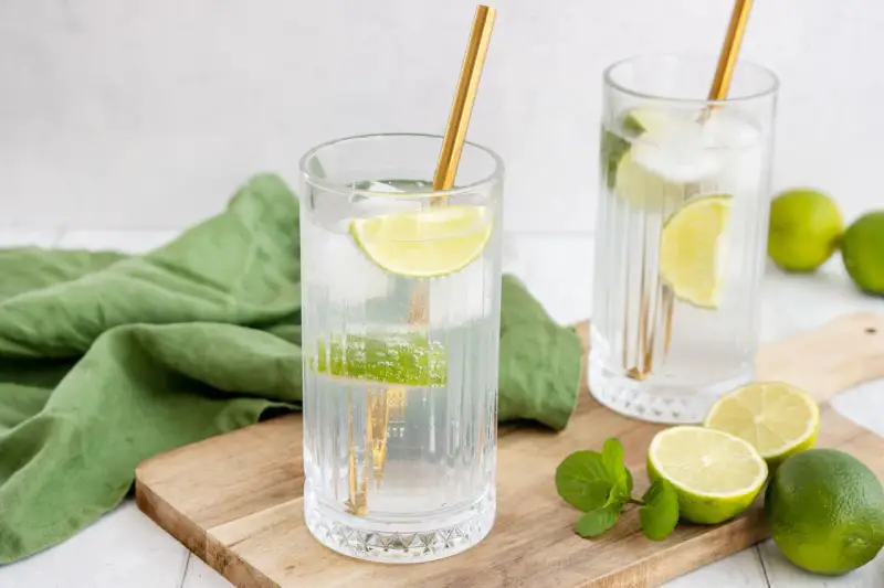 Erfrischende Drinks: Zwei Gläser mit Eis, Limettenscheiben und goldenen Strohhalmen. Perfekt zum **Wodka mischen** an einem warmen Tag.