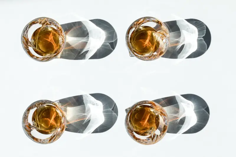 Vier Gläser mit bernsteinfarbenem Whisky werfen dramatische Schatten. Ein visueller Vergleich, der den Unterschied Scotch und Bourbon verdeutlicht.