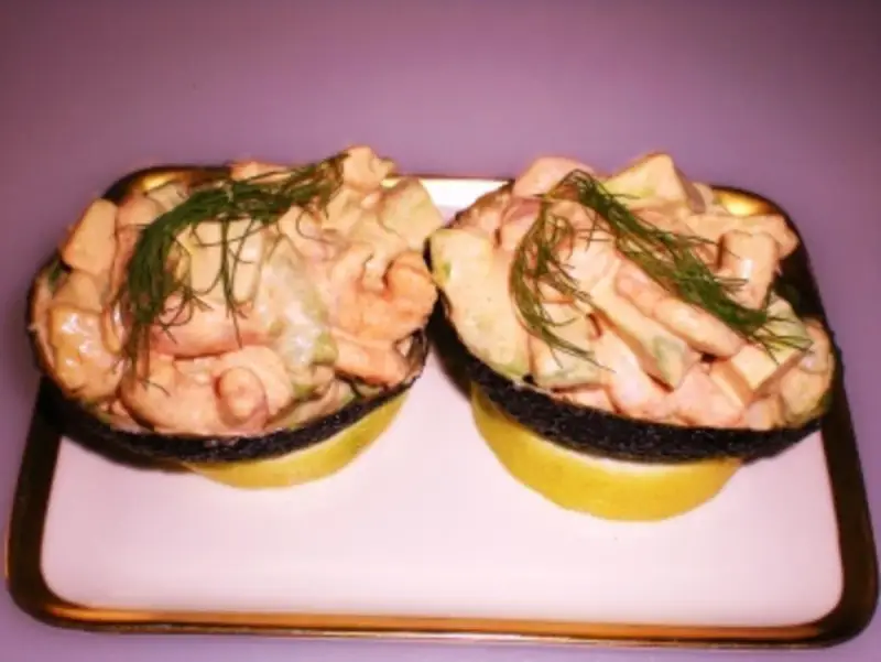 Zwei Avocadohälften gefüllt mit einem cremigen Krabbencocktail mit Avocado und Dill garniert, serviert auf Zitronenscheiben auf einem Teller.
